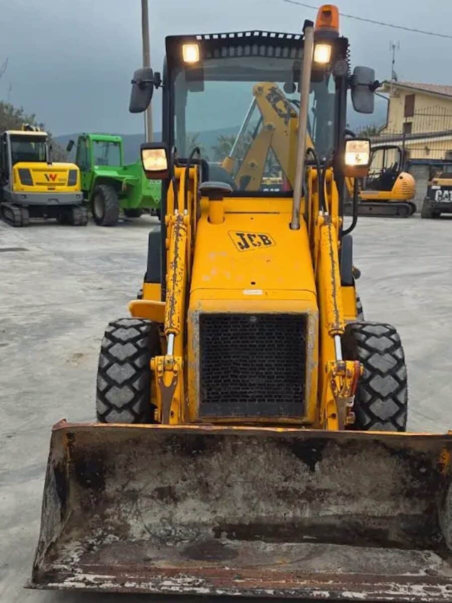 JCB 1CX con benna frontale in azione su terreno sterrato