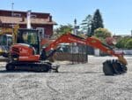 Mini-pelle Kubota KX57-4 vue latérale avec bras opérationnel et cabine fermée.