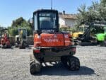 Vue frontale de la mini-pelle Kubota KX57-4 avec cabine fermée et lame avant.
