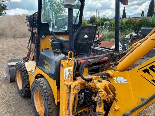 Vista posteriore laterale della JCB 1CX con stabilizzatori abbassati e impianto idraulico
