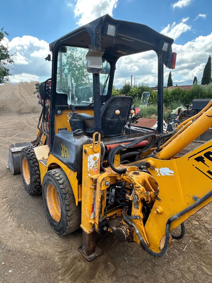 Vista posteriore laterale della JCB 1CX con stabilizzatori abbassati e impianto idraulico