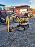 Komatsu PC09 usada, vista frontal derecha con pala niveladora y cazo de limpieza