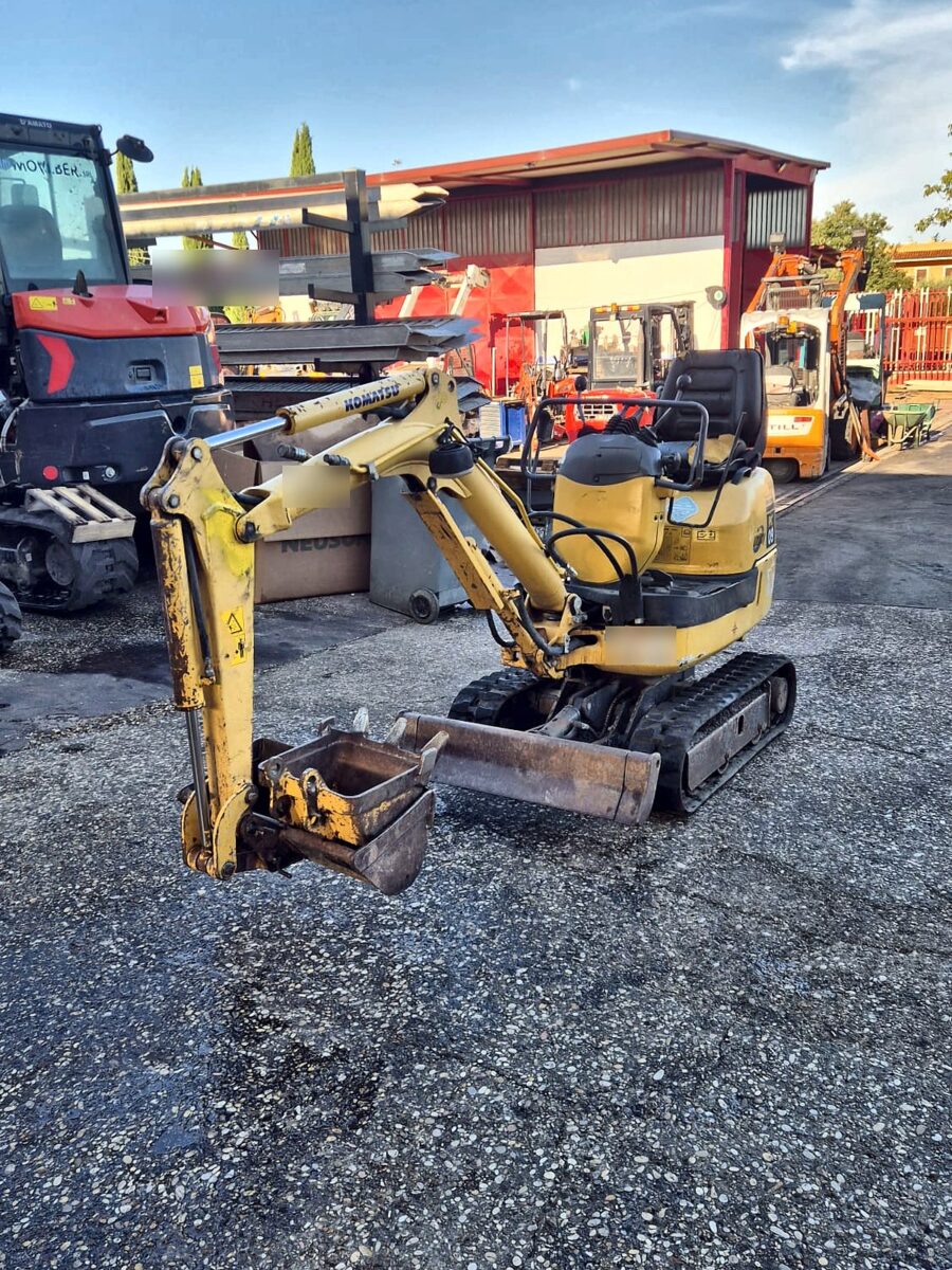 Komatsu PC09 usada, vista frontal derecha con pala niveladora y cazo de limpieza